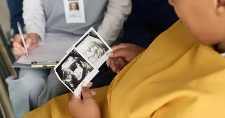 Frau mit dunkler Haut betrachtet zwei Ultraschallbilder einer Schwangerschaft.